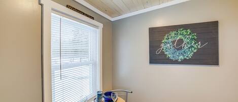 A dining area with a wooden table set for two, a window with blinds, and a wall-mounted sign that reads "Welcome to Home."