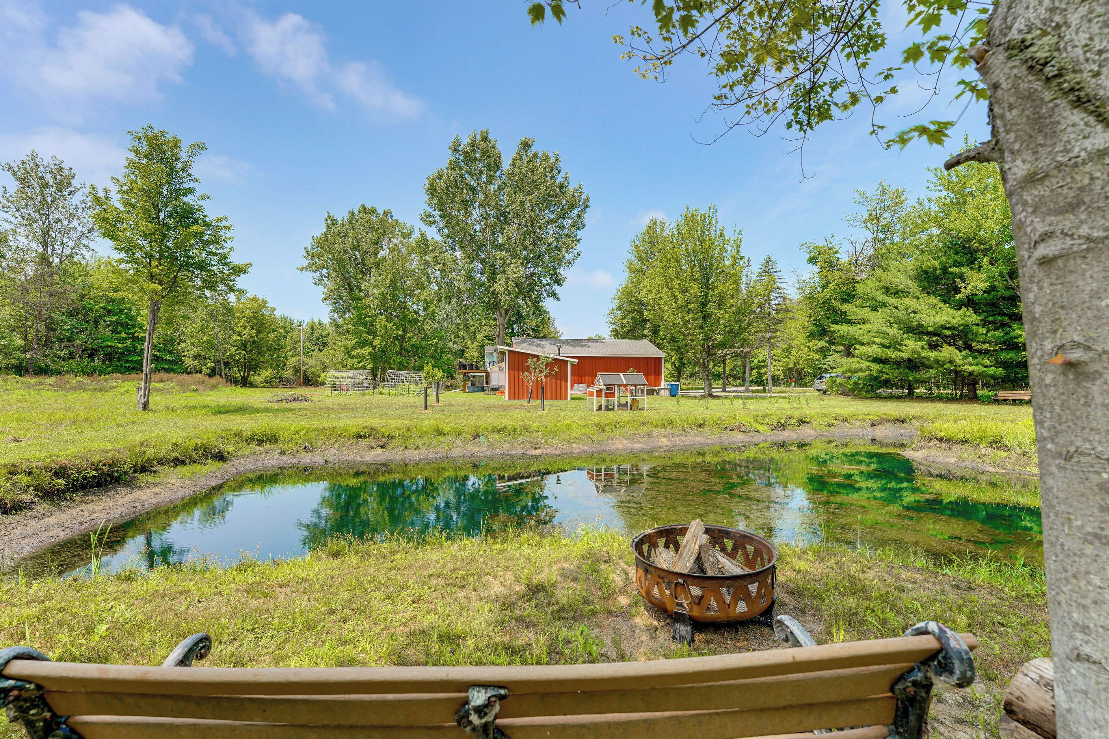 A bench by a pond with a red building in the background.