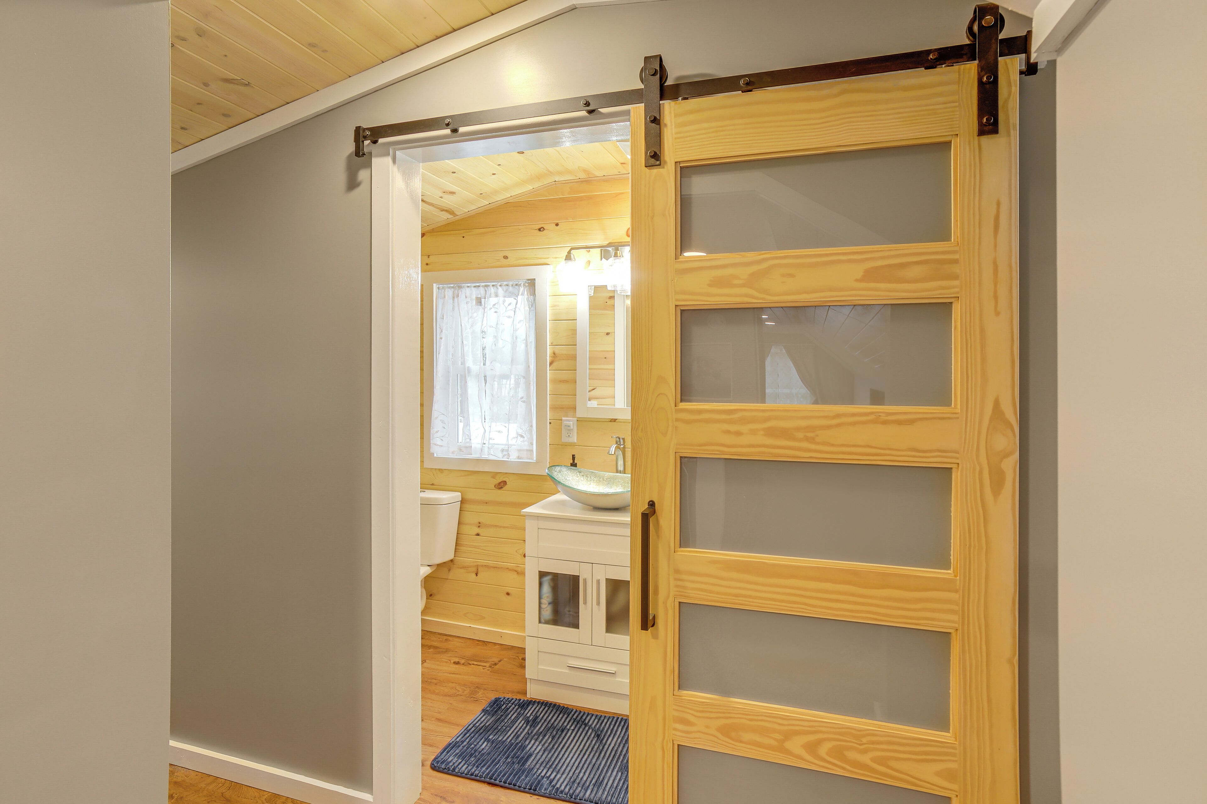 A wooden sliding door leading to a bathroom with a sink and cabinets.