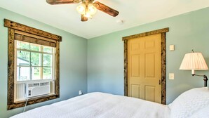 A bedroom with a bed, a ceiling fan, a window with an air conditioning unit, and a door. - Lake Pepin Cottage w/ Patio - Walk to the Marina! (Pepin)