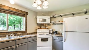 A kitchen with a double oven, microwave, and refrigerator. There is a window with a view of trees and a wooden beam above the sink. - Lake Pepin Cottage w/ Patio - Walk to the Marina! (Pepin)