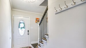 A hallway with a white door, a staircase with a black railing, and a wall-mounted coat rack. - Comfy Augusta Condo w/ Deck ~ 4 Mi to Olde Town (Augusta)