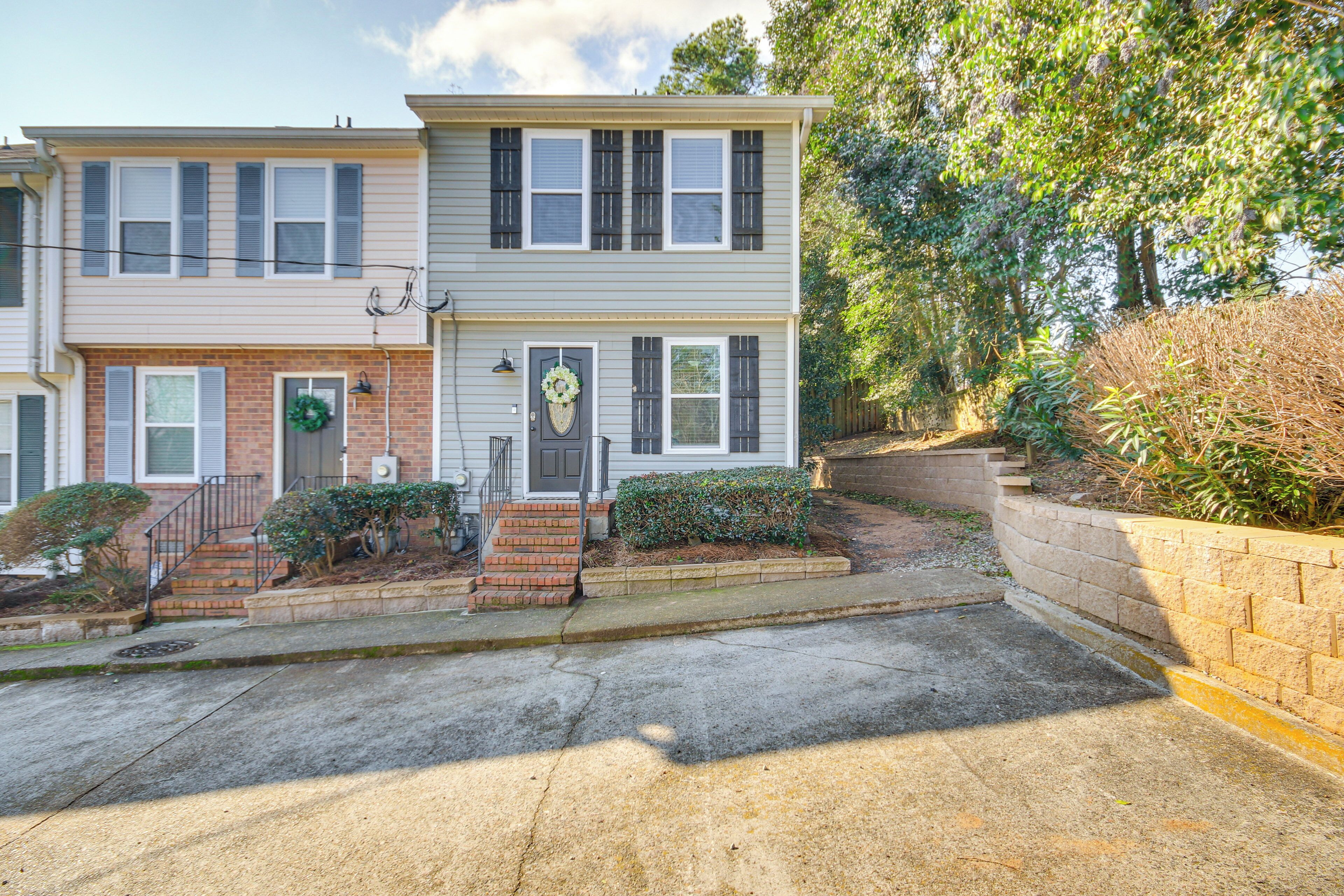 A two-story residential building with a front entrance, steps, and a small front yard with a brick planter and shrubs.