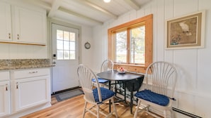 A dining area with a round table and four chairs, a window with a wooden frame, and a clock on the wall. - Cozy Harbor Springs Vacation Rental, 13 Mi to Town (Harbor Springs)