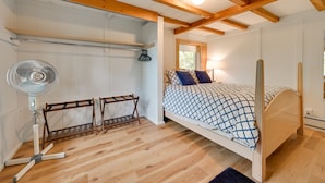 A bedroom with a wooden ceiling, a bed with a patterned bedspread, a standing fan, and a window with natural light. - Cozy Harbor Springs Vacation Rental, 13 Mi to Town (Harbor Springs)