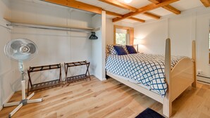 A bedroom with a wooden ceiling, a bed with a patterned bedspread, a standing fan, and a window with natural light. - Cozy Harbor Springs Vacation Rental, 13 Mi to Town (Harbor Springs)