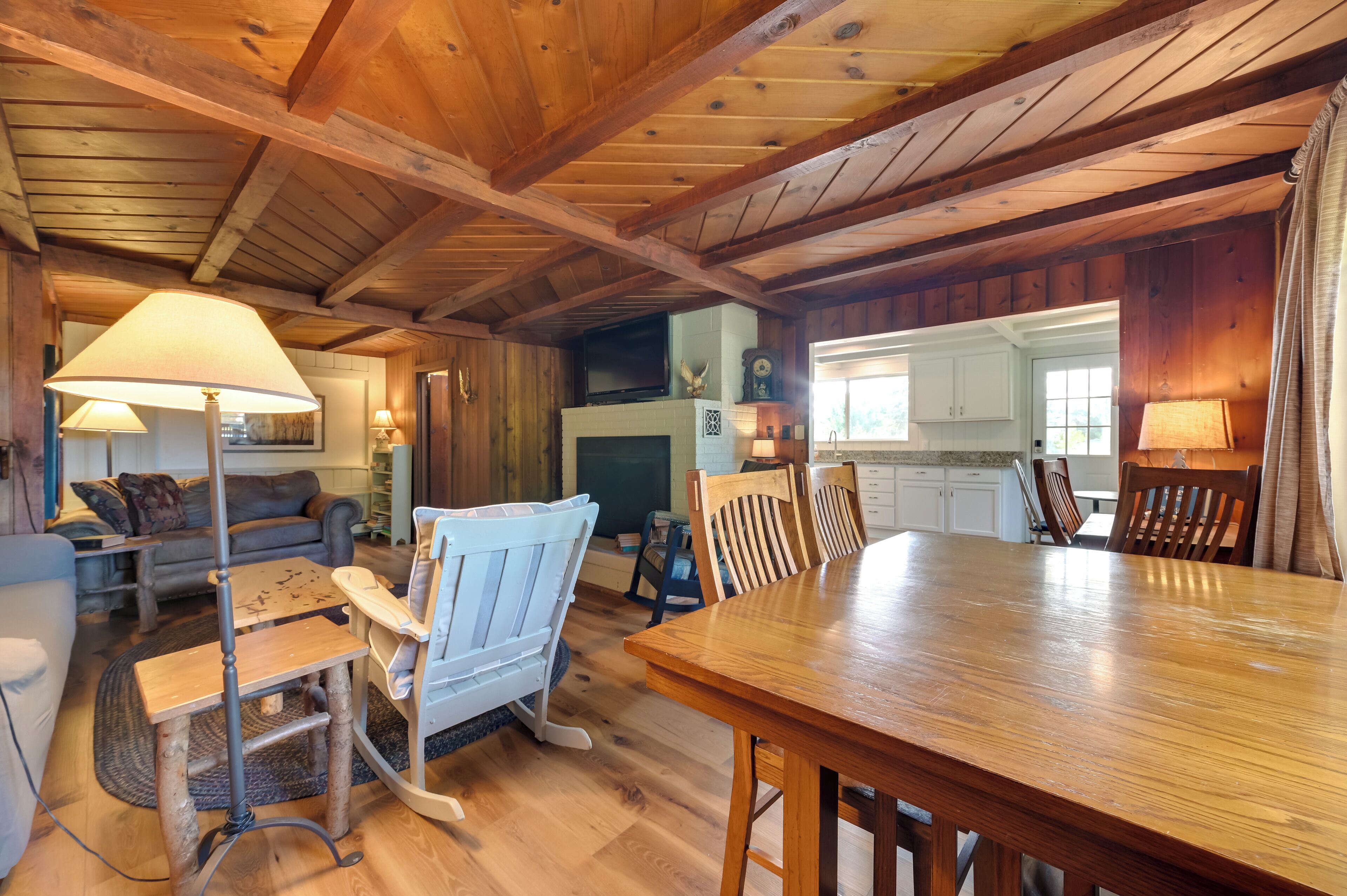 Interior rústico de uma cabana, com uma mesa de jantar de madeira, um sofá e uma lareira.