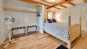 Un dormitorio con techo de madera, una cama con colcha estampada, un ventilador de pie y una ventana con luz natural.