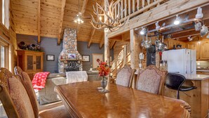 A wooden interior with a dining table, chairs, a fireplace, and a kitchen area.