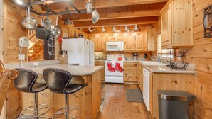 A wooden cabin-style kitchen with a central island, bar stools, and hanging pots.