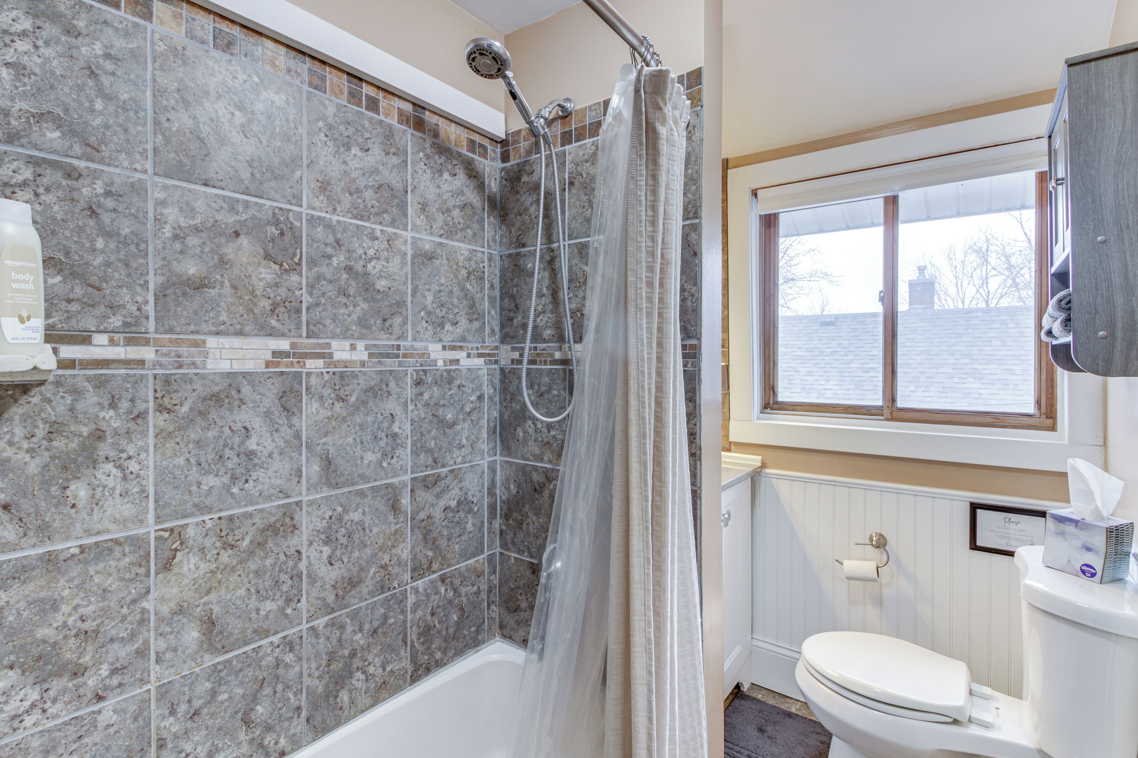 A bathroom with a shower, toilet, and a window.