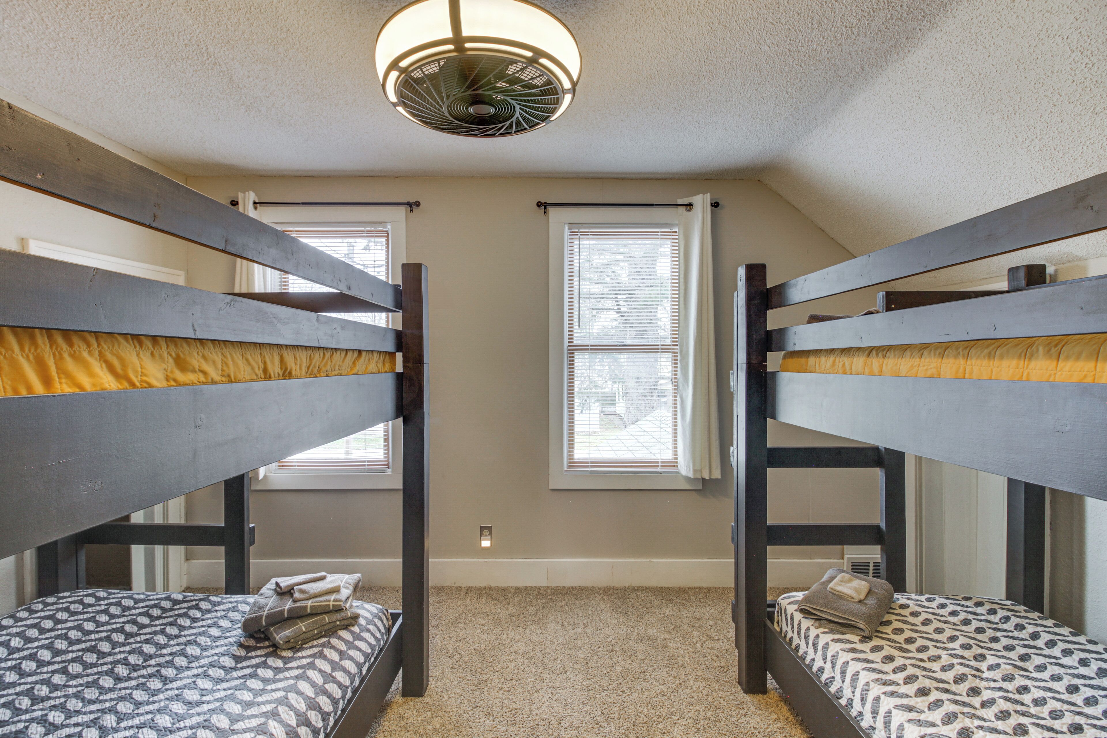 A room with two bunk beds, a ceiling fan, and two windows with blinds.