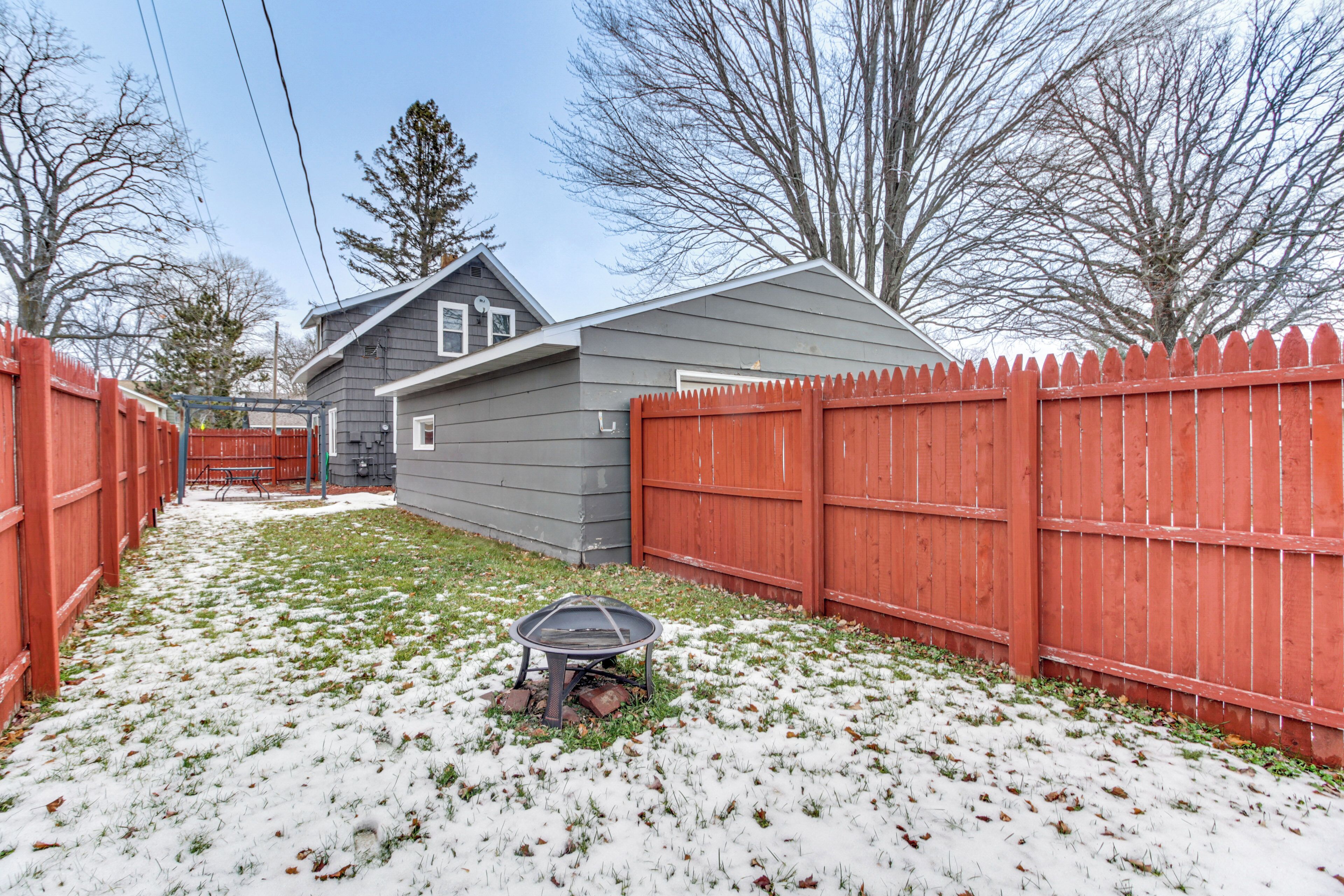 A backyard with a red wooden fence, a small shed, and a metal grill on the grass.