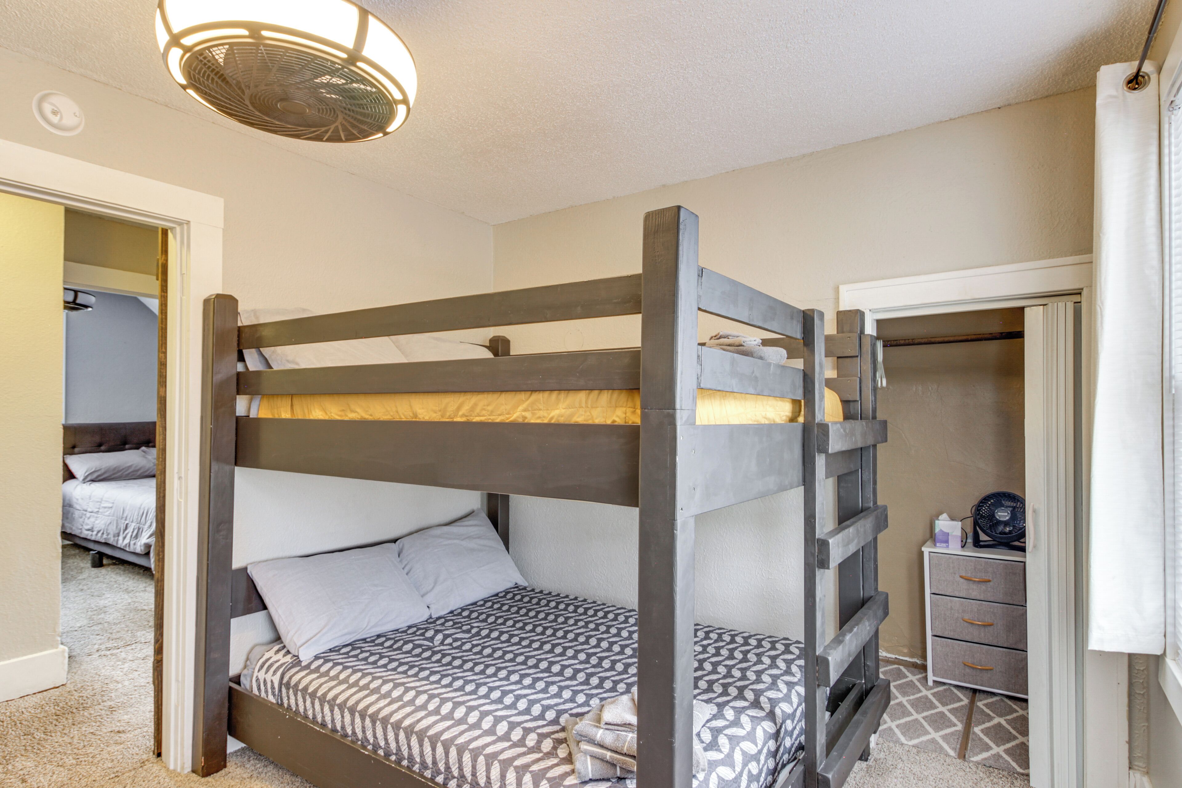 A bunk bed with a patterned bedspread, a bedside table with drawers, and a ceiling fan.