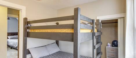 A bunk bed with a patterned bedspread, a bedside table with drawers, and a ceiling fan.