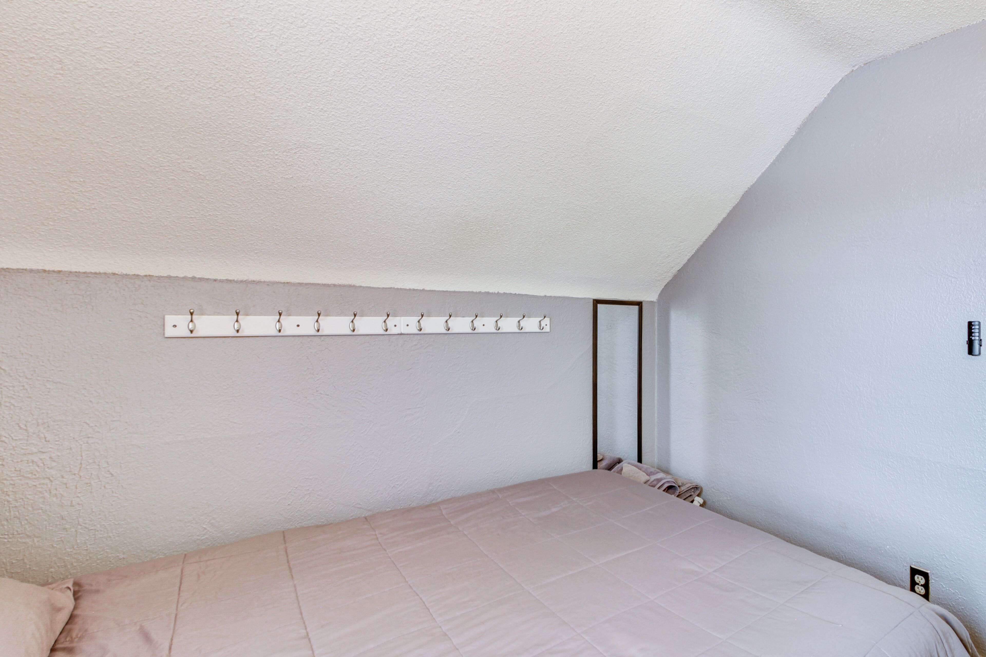 Un dormitorio con cama, perchero en la pared e interruptor de luz.