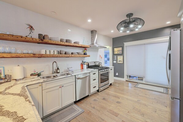 A modern kitchen with white cabinetry, a stainless steel stove, and wooden shelves above the counter.