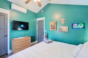 A bedroom with teal walls, a bed with white bedding, a wooden dresser, a mounted TV, and a wall-mounted heater.