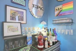 A bar area with various bottles and glasses, a clock, and framed artwork on the wall.