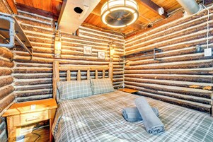 Una habitación tipo cabaña de madera con una cama, cabecera de madera y un ventilador de pared.