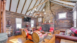 L’intérieur d’une cabane en rondins, avec un plancher en bois, un mur en pierre, un plafond en bois, un fauteuil à bascule en bois, un canapé, une table et un téléviseur.