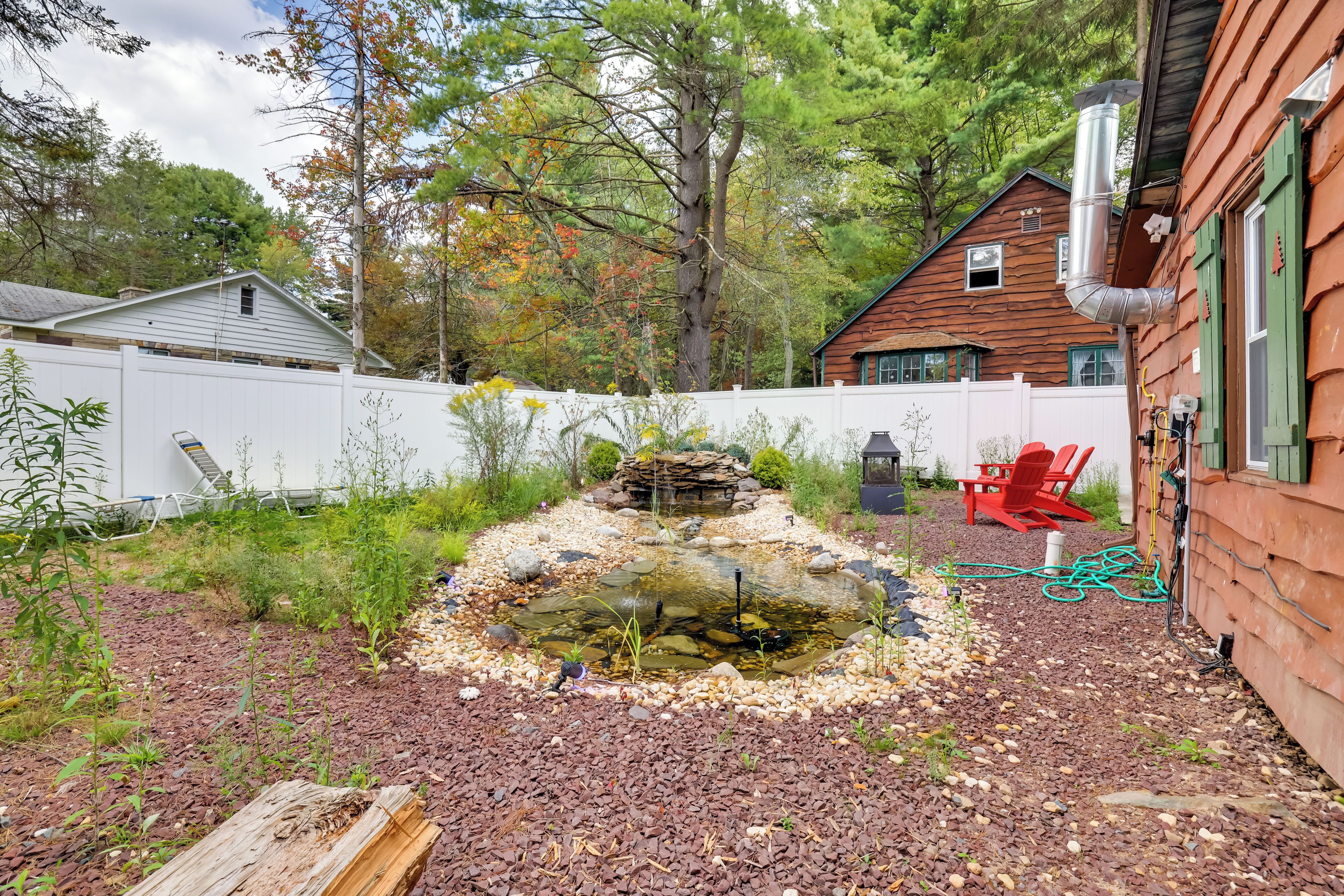 A backyard with a pond, wooden deck, and a red chair.
