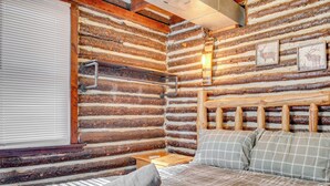 Une chambre à coucher située dans un chalet en rondins, avec un lit, des oreillers, une table de chevet et une fenêtre avec des stores.