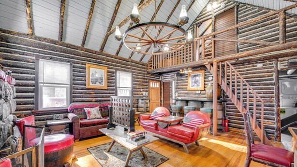 L’intérieur d’une cabane en rondins, avec un plancher en bois, un canapé en cuir rouge, une table basse en bois et un lustre.
