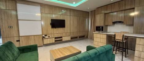 A modern living room with a green sofa, wooden cabinets, and a flat-screen TV.