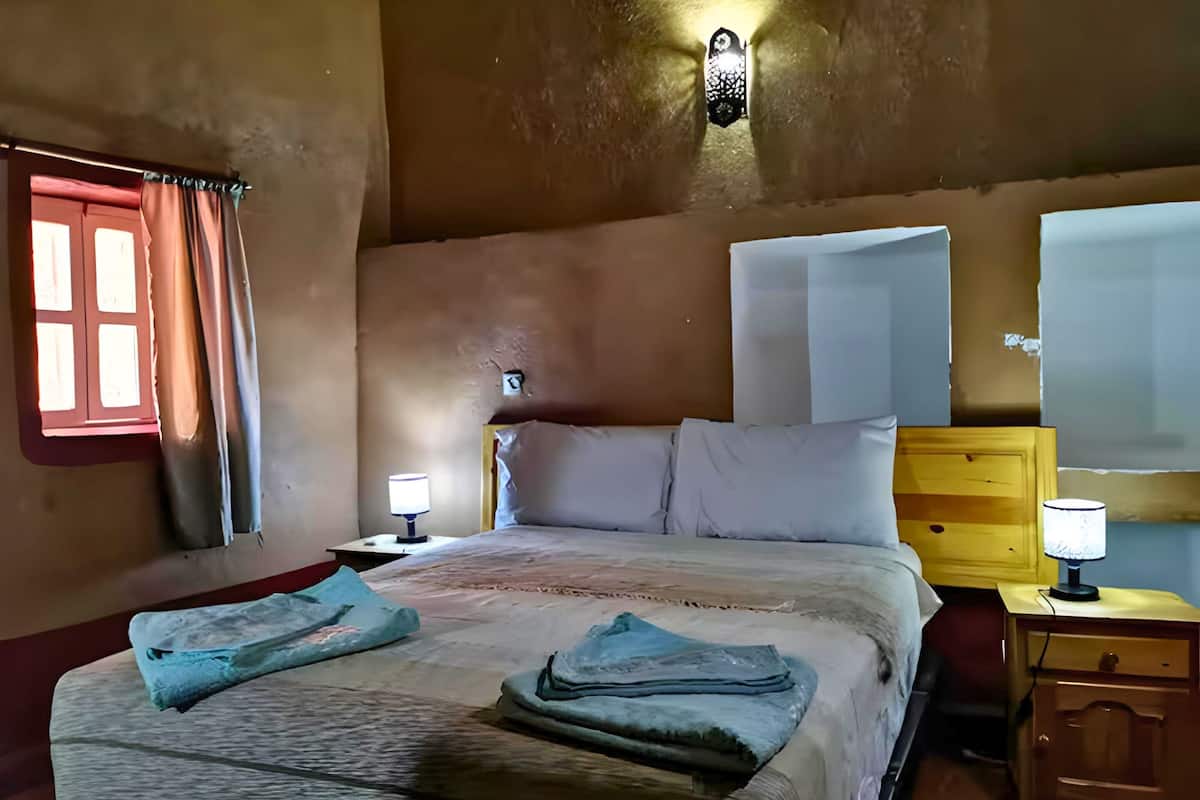 A bedroom with a bed, two bedside tables, a nightstand, and a wall-mounted lamp.