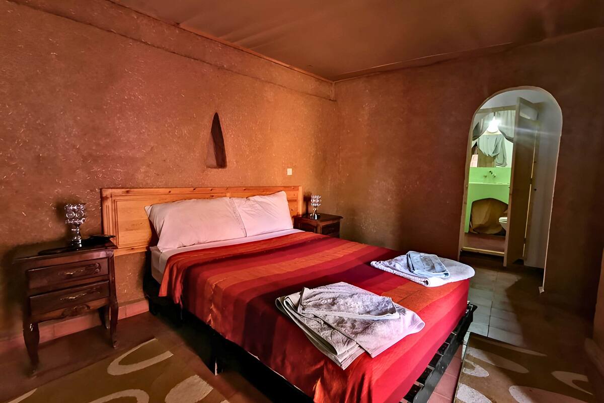 A bedroom with a wooden bed, a nightstand, a mirror, and a door leading to another room.