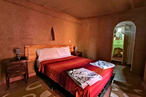 A bedroom with a wooden bed, a nightstand, a mirror, and a door leading to another room. - Riad dar zaouia (Zagora)