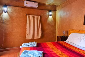 A room with a bed, a nightstand, a wall-mounted air conditioner, and two wall sconces. - Riad dar zaouia (Zagora)