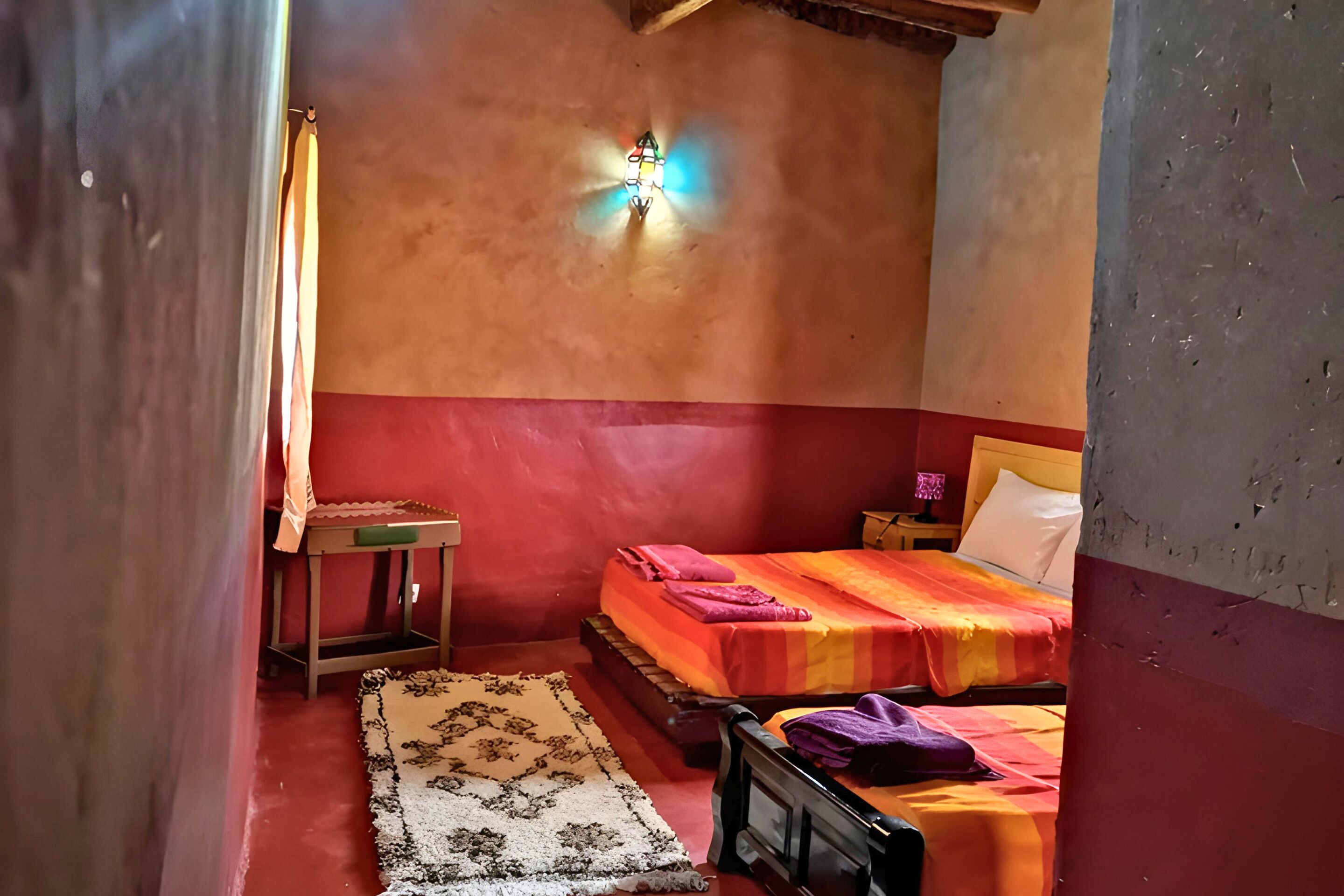 A small, cozy bedroom with a single bed, a nightstand, a lamp, and a patterned rug.