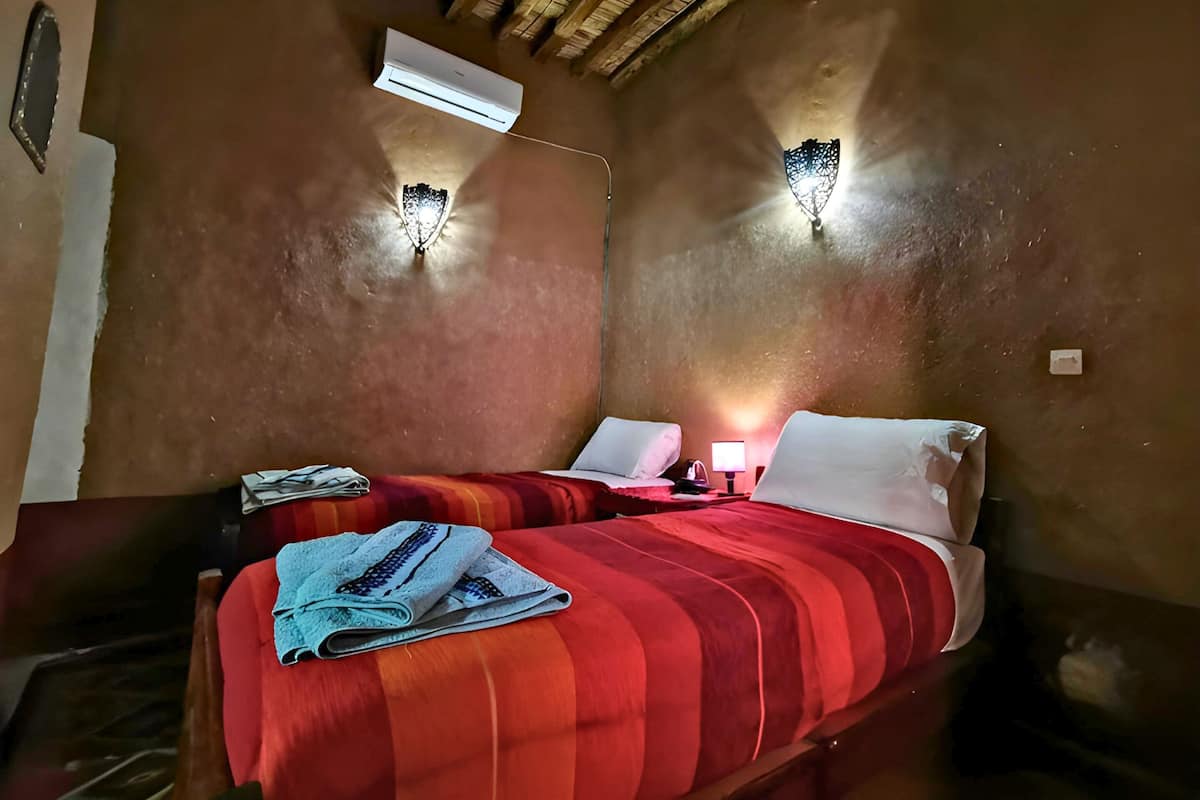 A room with two beds, each with red and white bedding, a small table with a lamp, and wall-mounted light fixtures.
