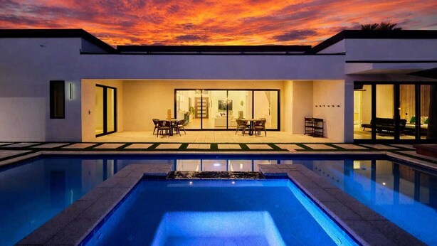 A modern house with a swimming pool, a patio with outdoor furniture, and a glass door leading to an interior space.