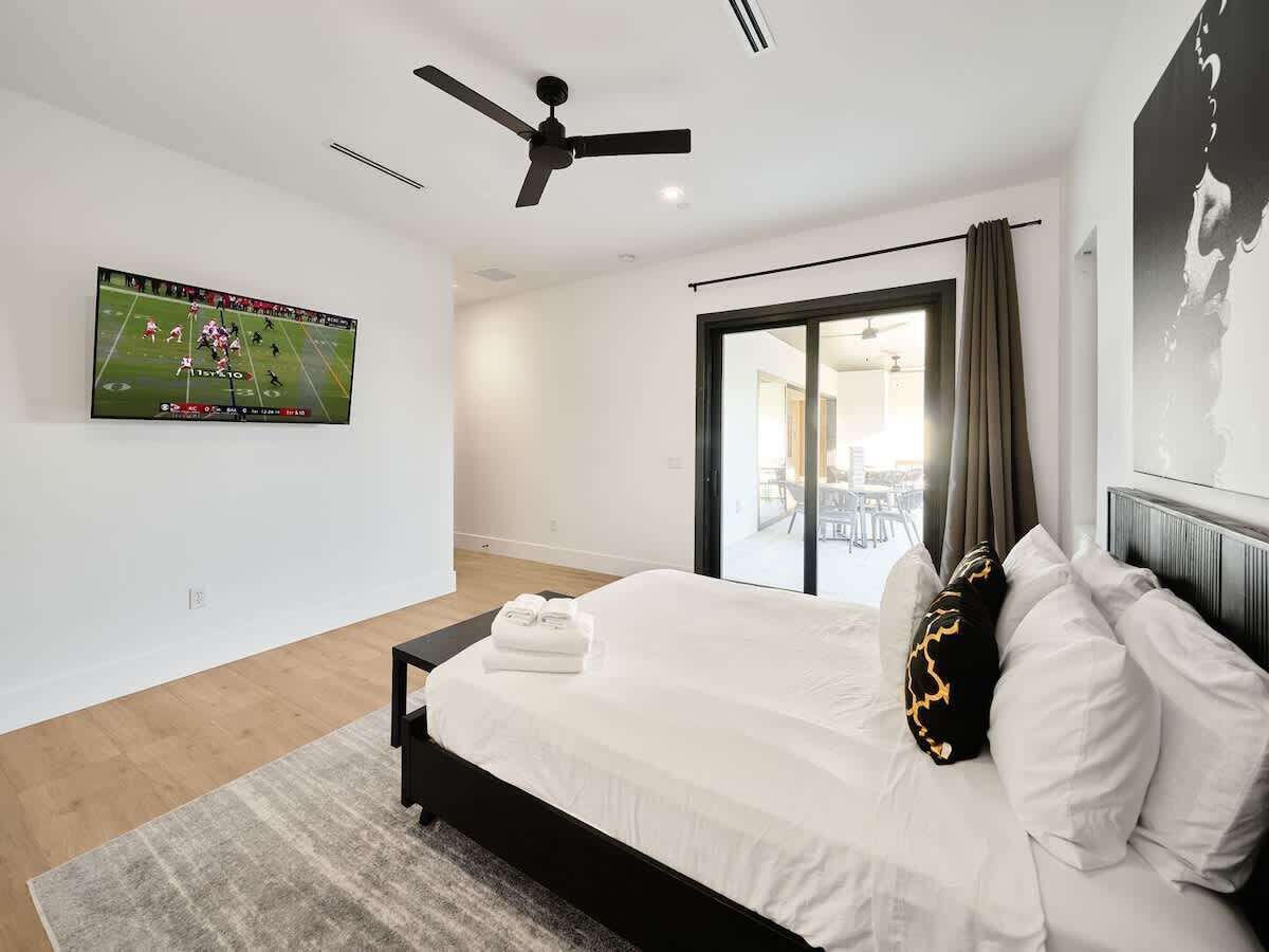 Un dormitorio moderno con cama, ventilador de techo, televisor en la pared y vistas al exterior.
