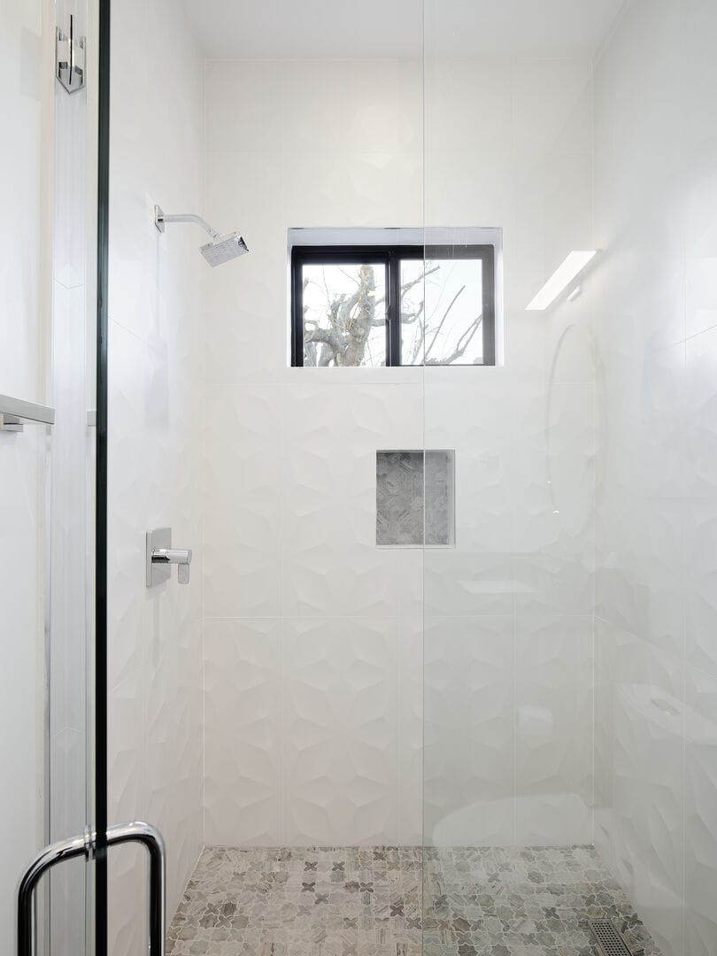 A shower with a window, a door, and a tiled floor.