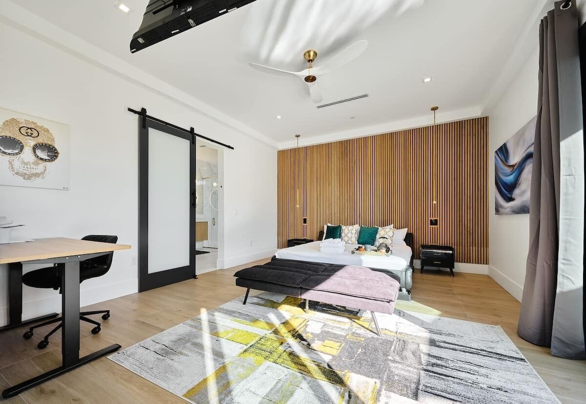 Un dormitorio moderno con cama, mesitas de noche, escritorio y un amplio ventanal.
