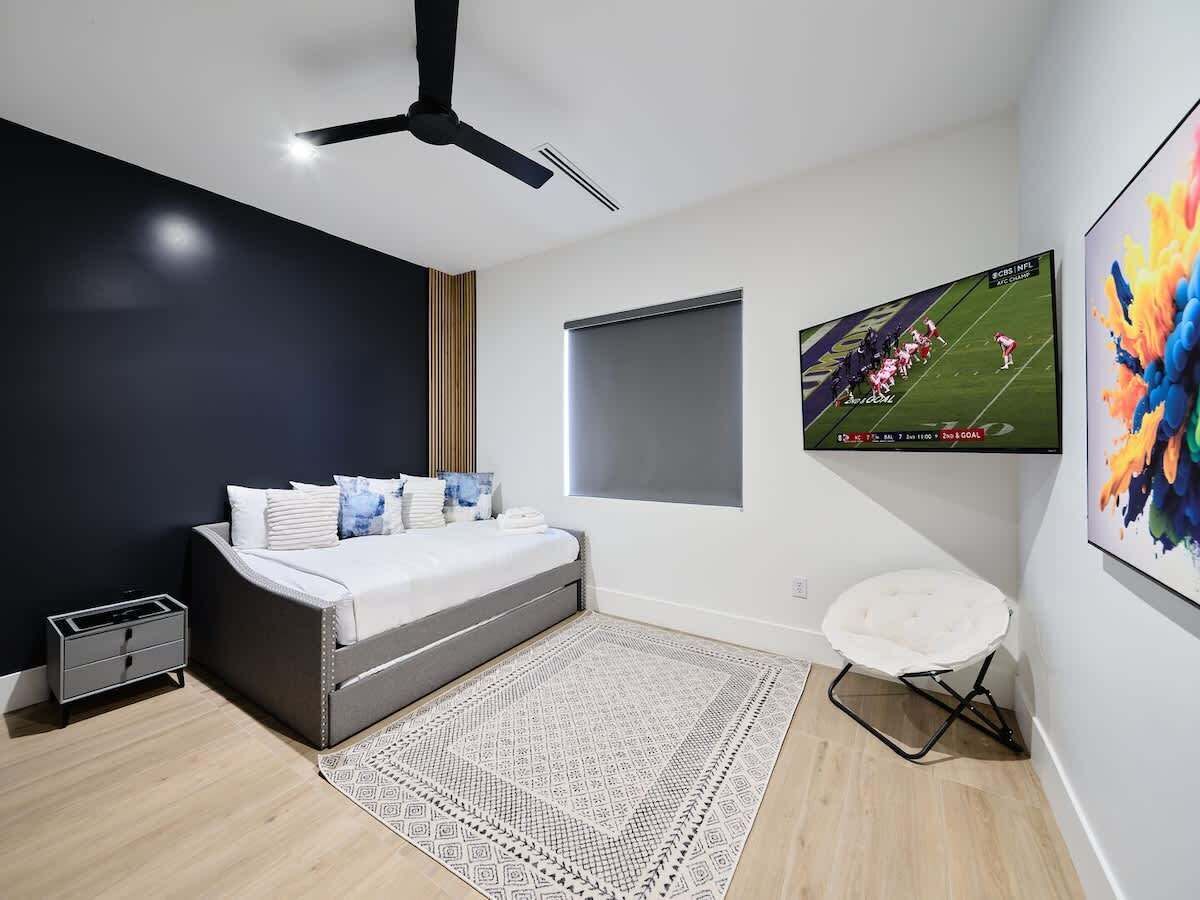 A modern bedroom with a bed, a ceiling fan, a TV, and a wall-mounted artwork.