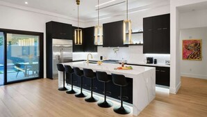 A modern kitchen with a central island, black bar stools, and pendant lighting.