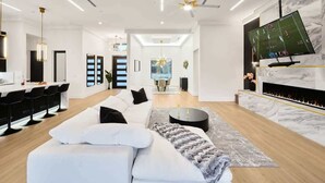 A modern living room with a white sofa, a fireplace, a TV, and a dining area with black chairs.