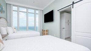 A bedroom with a large bed, a TV, a wardrobe, and a view of the ocean. - Phoenix Gulf Towers 1908 4 Bedroom Condo (Orange Beach)