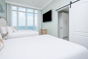 A bedroom with a large bed, a TV, a wardrobe, and a view of the ocean.