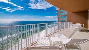 Ein Balkon mit weißen Stühlen und Tischen, der auf einen Strand und den Ozean blickt.