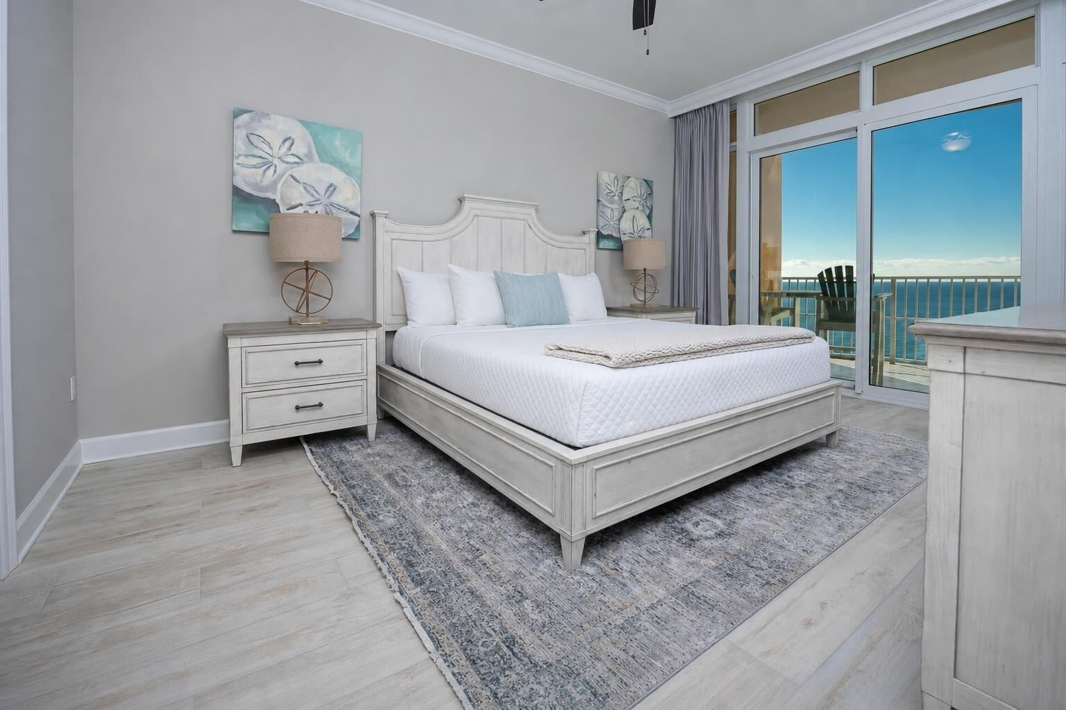 A bedroom with a bed, nightstands, a rug, and a view of the ocean through a balcony.