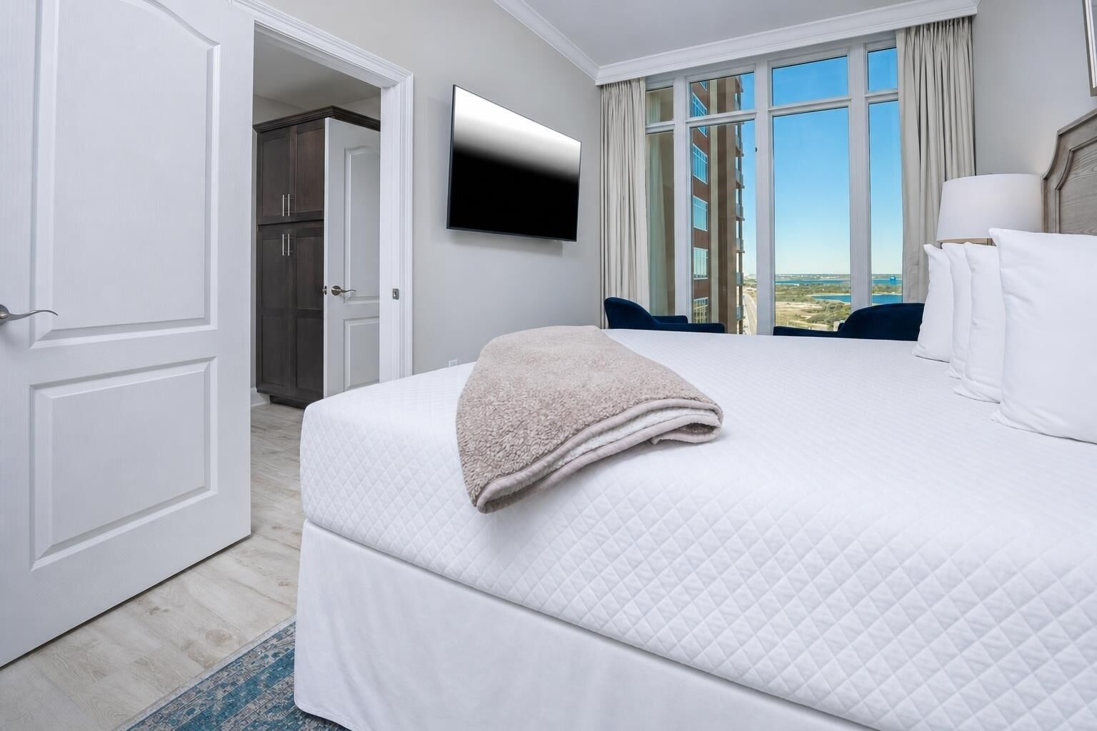 A hotel room with a bed, a television, a window with a view, and a door leading to another room.