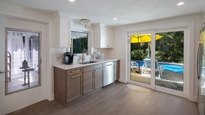 A modern kitchen with a large island, a built-in oven, and a view of a swimming pool through glass doors. - Mermaid's Treasure 2 Bedroom Home by RedAwning (Anna Maria)