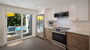 A modern kitchen with white cabinets, stainless steel appliances, and a glass door leading to a pool area. - Mermaid's Treasure 2 Bedroom Home by RedAwning (Anna Maria)