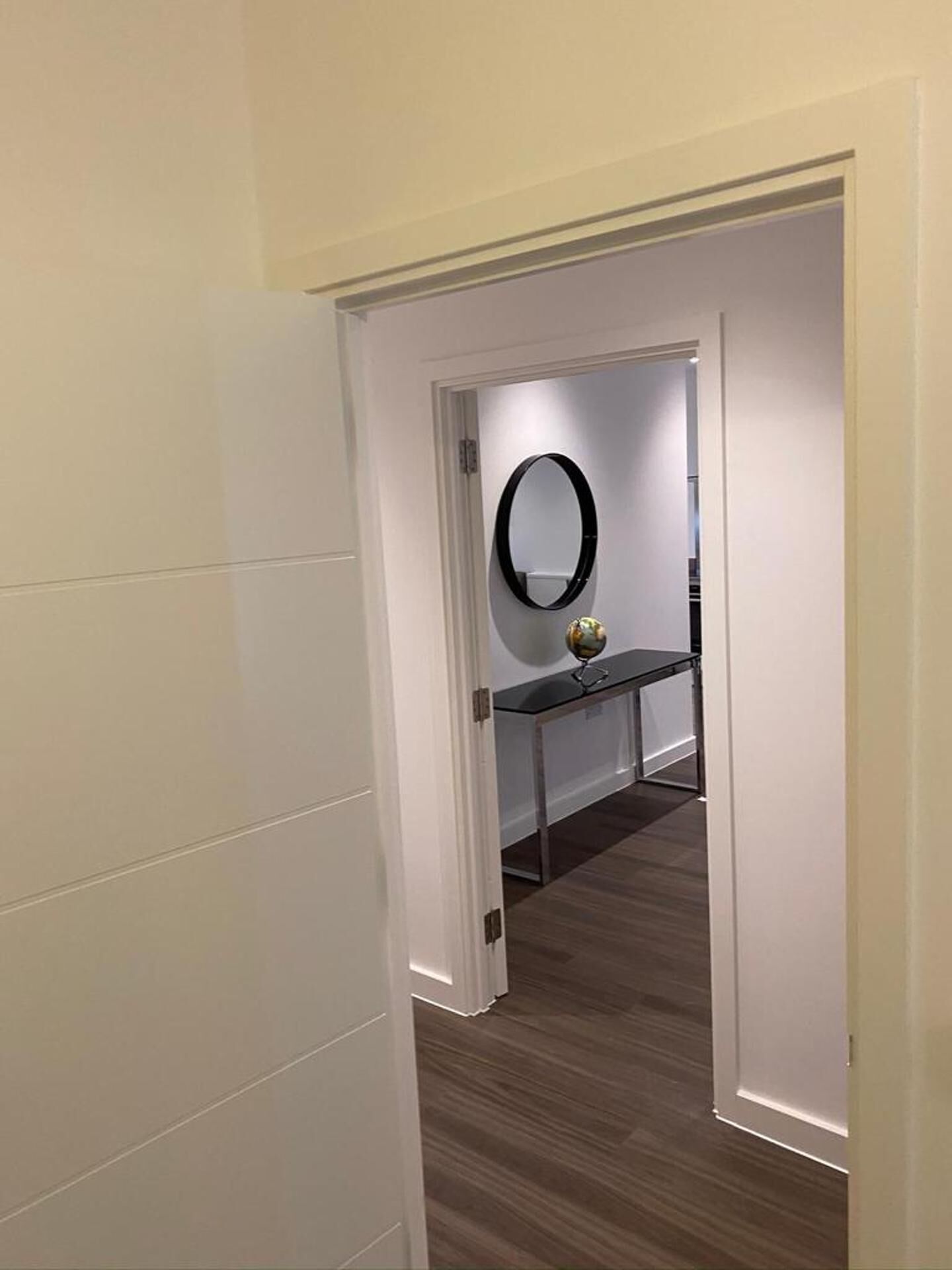 A hallway with a white door leading to a room with a mirror and a small table with a decorative item.